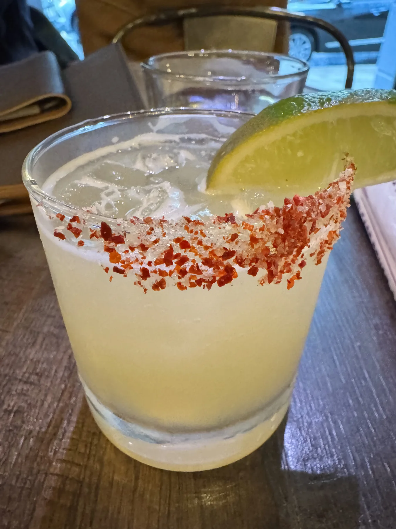 A cocktail with a chili-salt rim and lime wedge on a wooden table