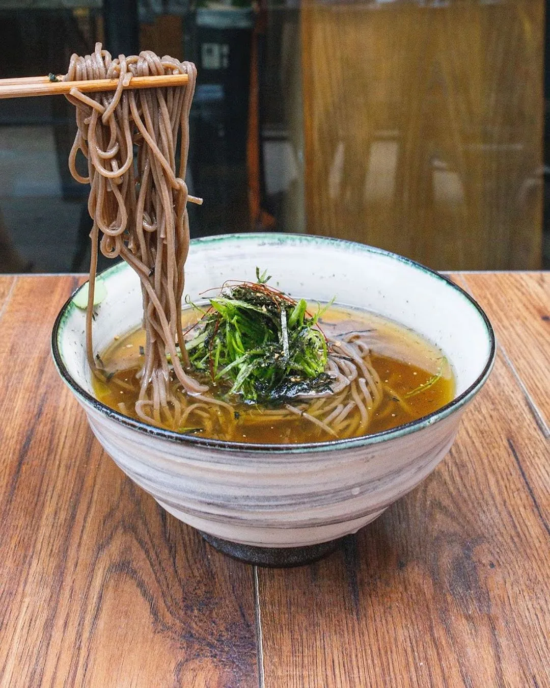 Soba noodles in amber broth lifted with chopsticks